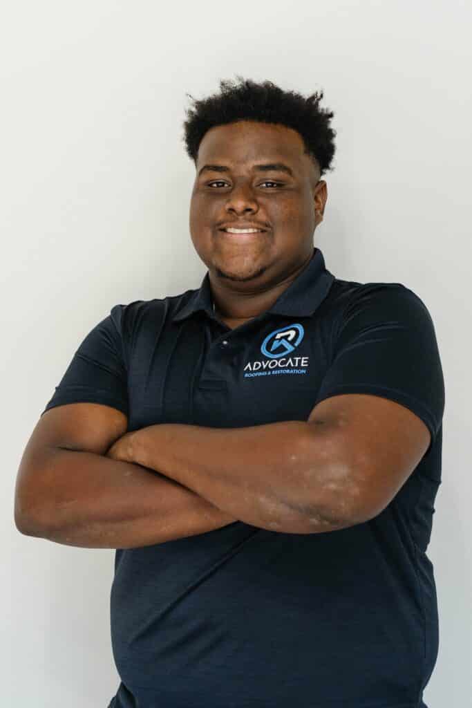 A person in a blue polo shirt is standing with arms crossed, smiling at the camera against a white background. They have short, dark hair.