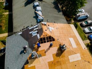 An aerial view showing several people working on a large, partially completed roof with materials and tools scattered around on a sunny day.